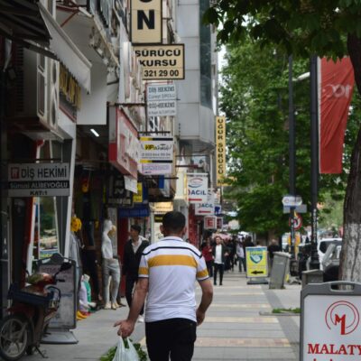 Vibrant street in Malatya, Türkiye with people walking past shops and signs.